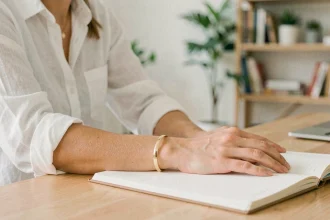 Femme portant un bracelet or jonc au quotidien dans un bureau minimaliste, associé à une chemise en lin blanche